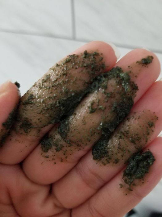 A reviewer demonstrates the texture of the green, gritty scrub in their hand.