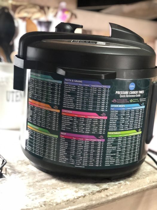 A pressure cooker with a detailed chart on its side displaying cooking times for pasta, grains, chicken, beef, and vegetables.