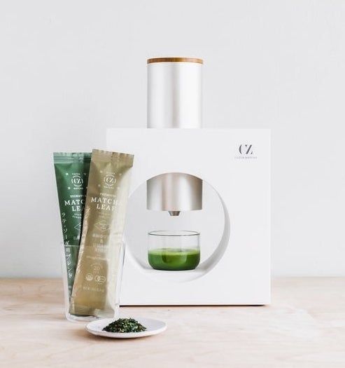 The sleek white appliance resting next to matcha leaf packets, ready to brew.