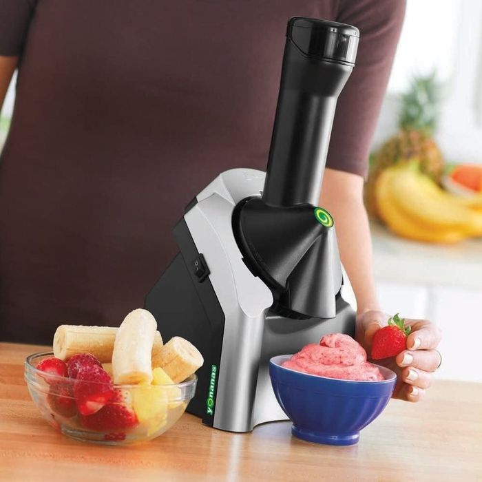 A model placing a fresh strawberry on top of a bowl of soft serve under the Yonanas machine.