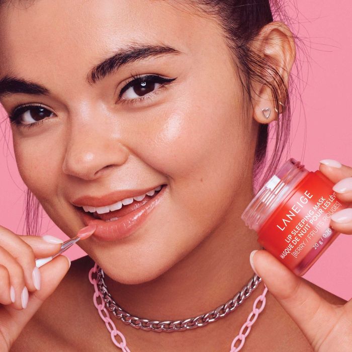 A model holding the scrub jar and using an applicator to apply it to their lips