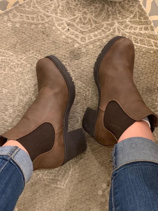 A photo of the brown ankle boots with chunky heels worn over cuffed jeans on a textured carpet, shared by a reviewer