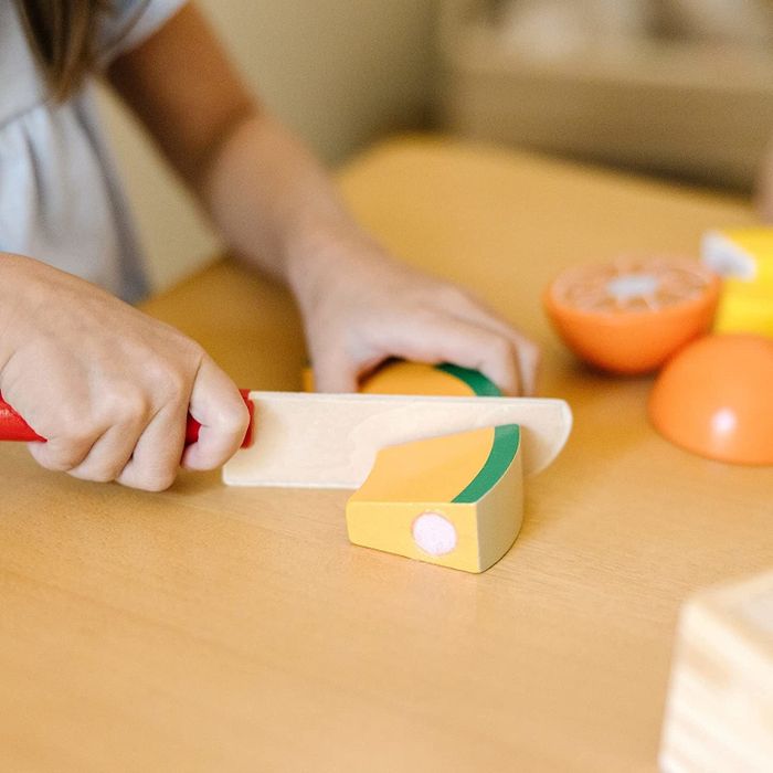 Child slicing a cantaloupe with the wooden fruit set