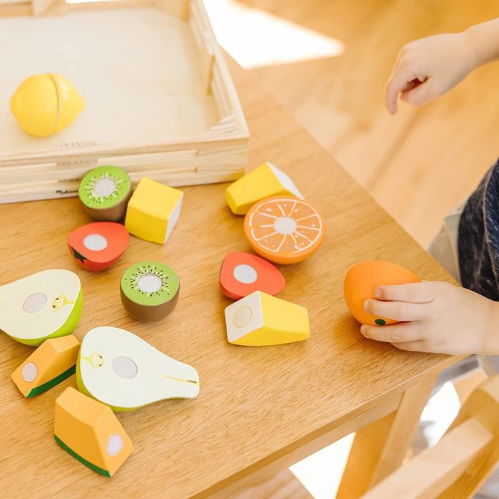 A wooden display of various fruits on a table, including kiwi, pears, oranges, bananas, cantaloupe, strawberries, and a lemon