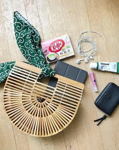 The bamboo handbag is accessorized with a scarf and packed with various items inside.