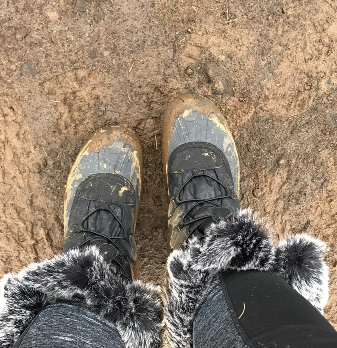 The reviewer is seen wearing boots that are covered in mud.