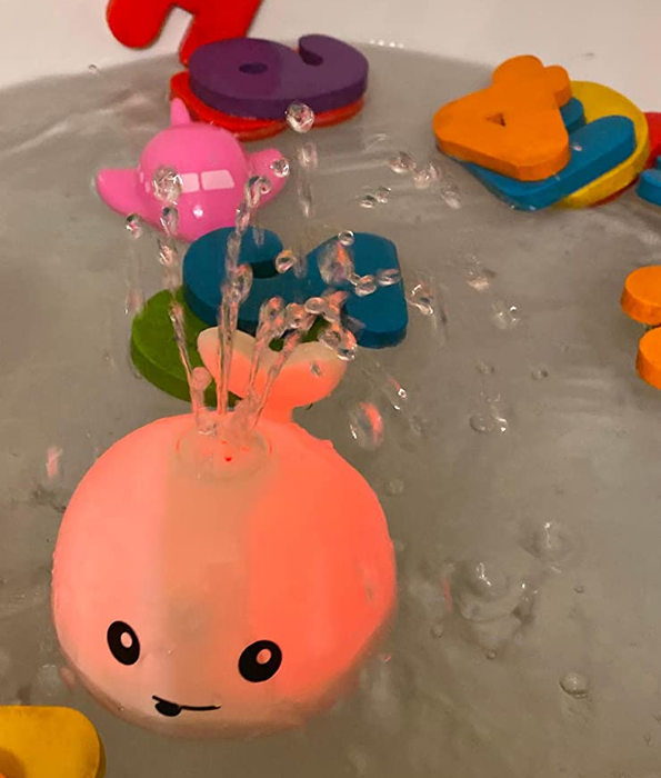 A reviewer’s photo of the whale bath toy glowing and spraying water in the tub