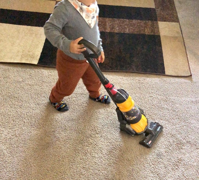 A photo of the reviewer’s child using the mini Dyson vacuum on a carpet