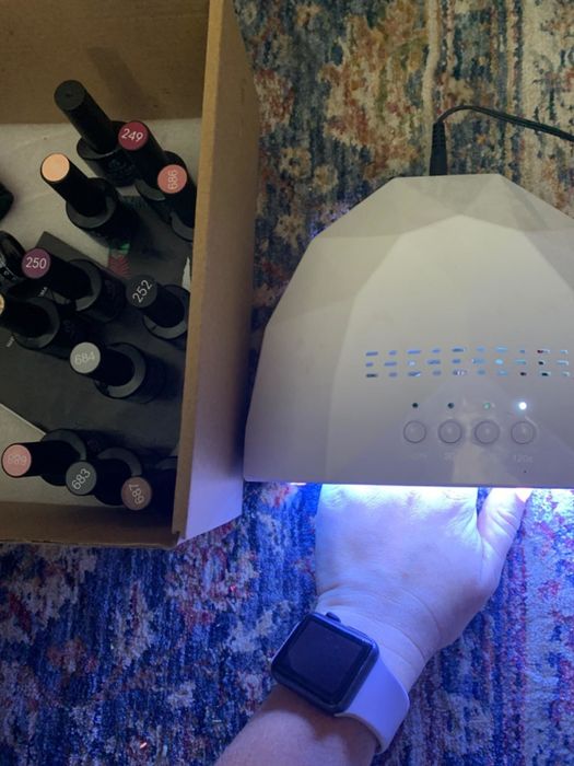 A reviewer demonstrating how to dry their gel nail polish under a UV light, with their hand positioned underneath.