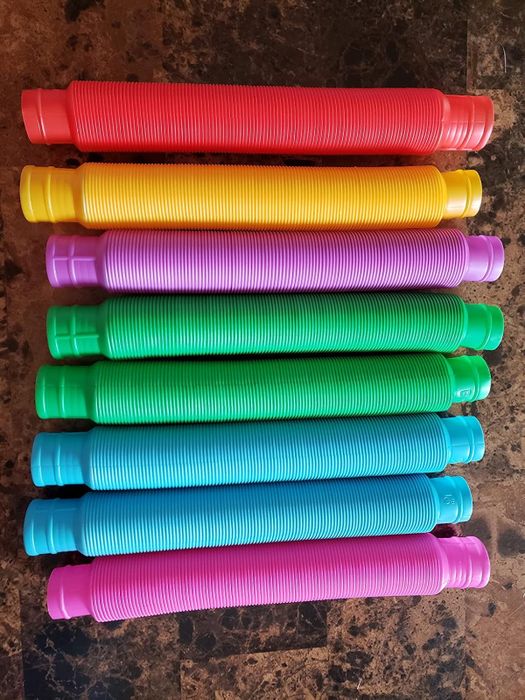 Eight colorful sensory pop tubes arranged in a row on a textured surface