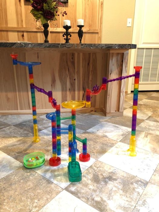 A vibrant marble run set assembled on a tiled floor, with a bowl of marbles nearby