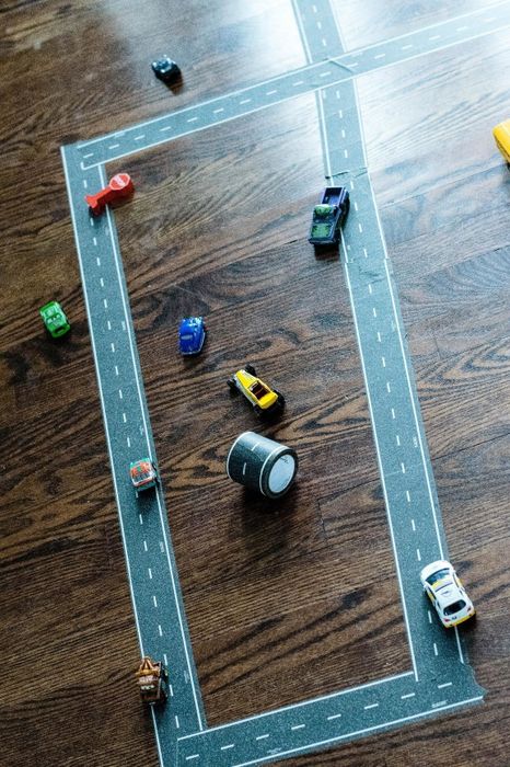 Toy cars lined up on a tape road layout spread across a wooden floor, showcasing a fun, creative setup for children