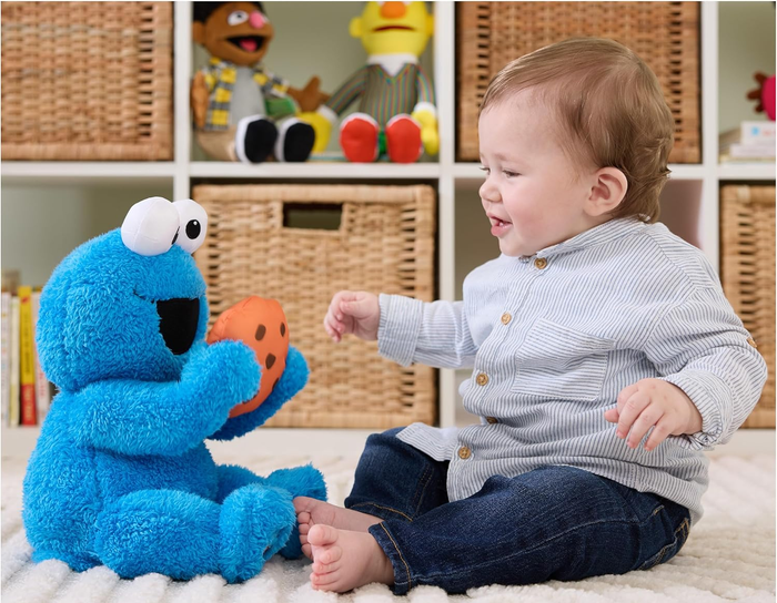A baby playing with a Cookie Monster toy in a nursery. Text: