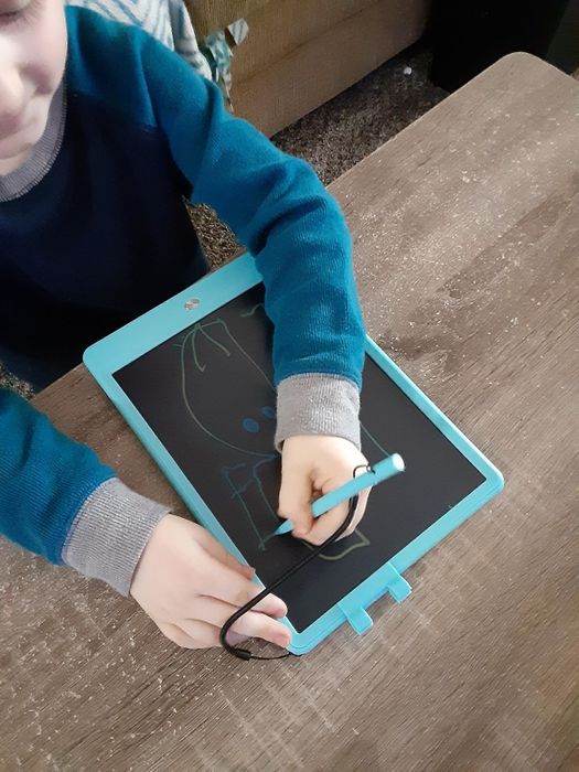 A child drawing on an LCD writing tablet, showing off a tech gadget that's perfect for kids