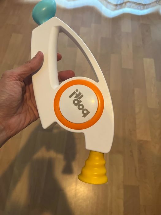 A person enjoying the fun with a modern Bop It! toy, featuring a playful blue, white, and yellow handle, designed for easy use during shopping.