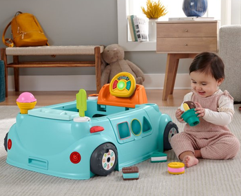 A baby sitting beside an ice cream truck-themed toy.
