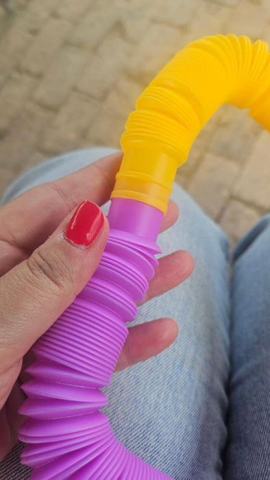A hand holding a flexible fidget toy with a ribbed texture, in purple and yellow