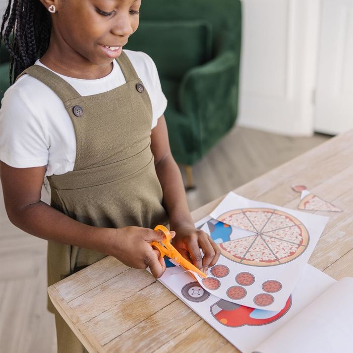 A child using scissors to cut out food shapes from paper, engaged in a craft activity at a table