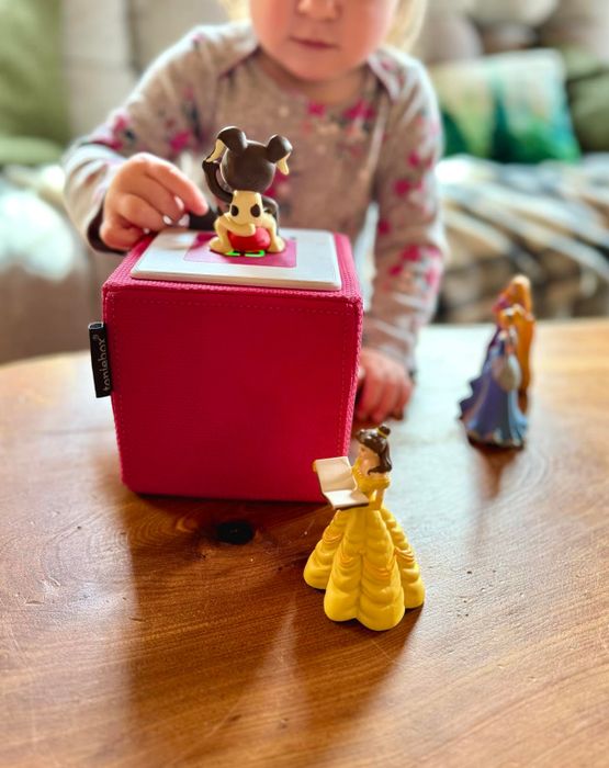 A child interacting with a Toniebox on a table, surrounded by figurines of Disney characters.