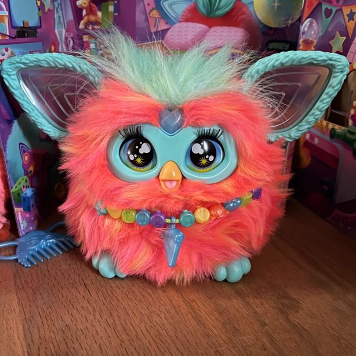 A colorful toy creature with large eyes, soft fur, and a beaded necklace, set in a playful environment