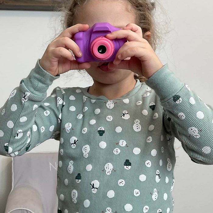 A child in a patterned sweater playfully holds a toy camera up to their face