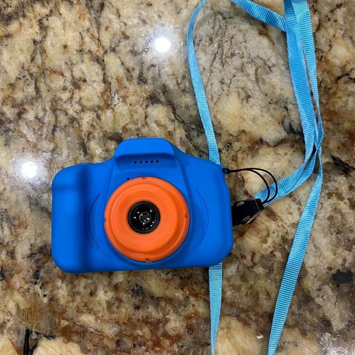 A blue toy camera for kids featuring an orange lens and a matching blue strap, resting on a granite countertop