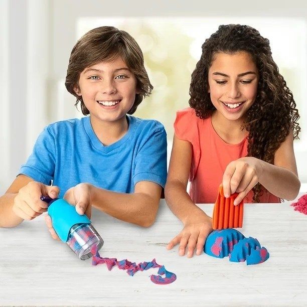 Two kids having fun playing with kinetic sand, creating shapes and designs