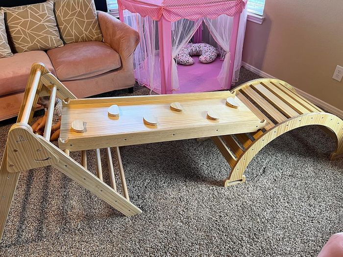 A children's wooden playset with slides and climbing structures, set up in a living room beside a pink play tent.
