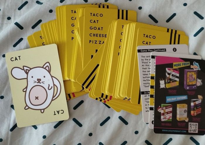 A spread of yellow Taco Cat Goat Cheese Pizza game cards scattered across a dotted surface, with several instructional and promotional cards visible