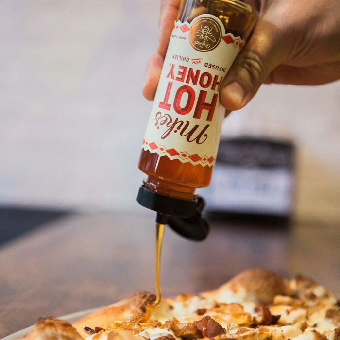 The honey being poured over a delicious pizza slice.