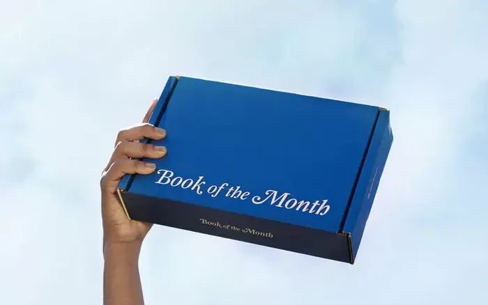 A hand holding a cardboard box labeled 'Book of the Month'
