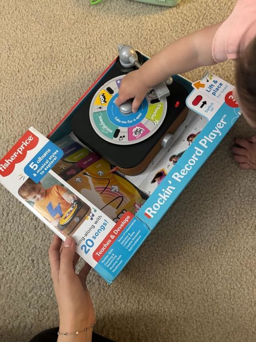 A child playing with the Fisher-Price Rockin' Record Player toy, which features 5 albums and 20 songs. The playful and educational design is perfect for young children.