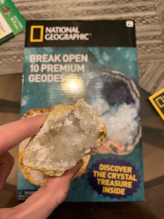 A hand holds an open geode in front of a box.