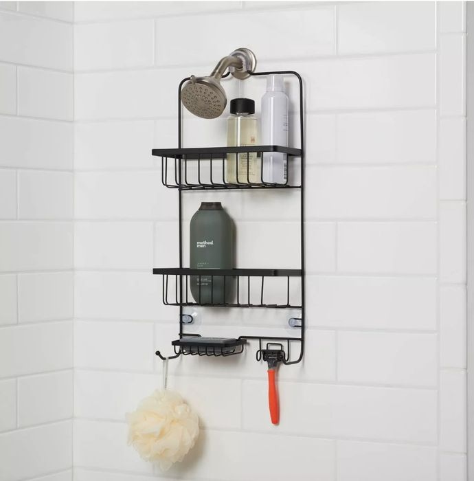 The black shower caddy resting against white tile, filled with a razor, sponge, and bottles.