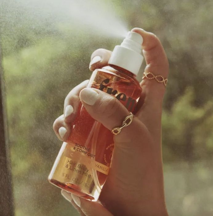 a hand holding a spray bottle, releasing a mist