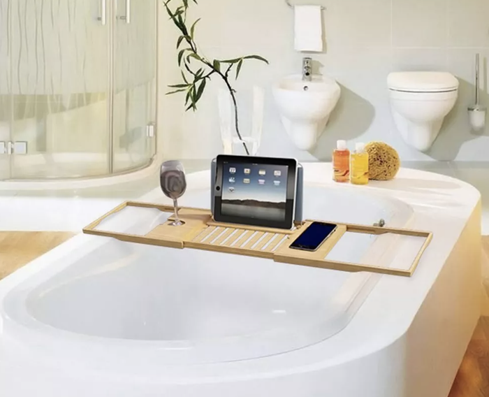 A bamboo bath caddy placed over a white tub, holding a tablet and a glass of wine.