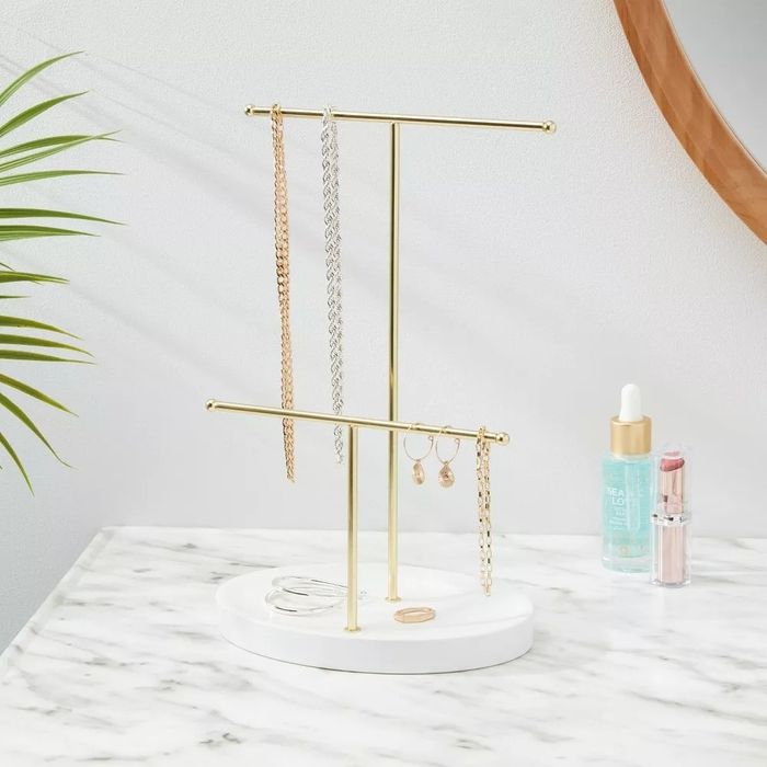The jewelry stand, placed on a bathroom counter, is neatly organized with necklaces and earrings.