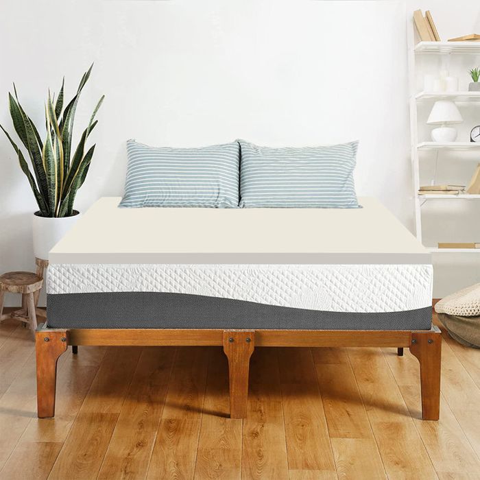 A tidy bed adorned with striped pillows, set on a two-tone mattress in a modern, minimalist bedroom with plants and floating shelves.