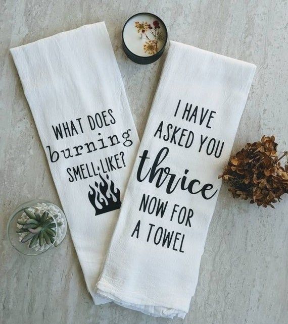 A white tea towel that reads 'What does burning smell like?' with a small flames icon, and another that says 'I have asked you thrice now for a towel'.