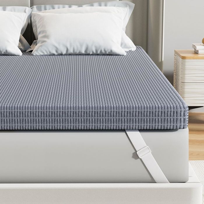 A grey mattress topper with a textured ribbed pattern, placed on a bed with white pillows, set in a sleek, modern bedroom.