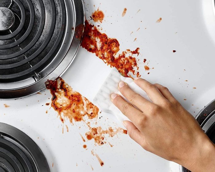Someone is cleaning food off a stovetop using a sponge.