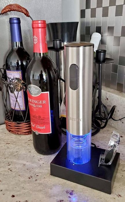 A review photo showing the electric corkscrew resting on its charging dock next to the included foil cutter.