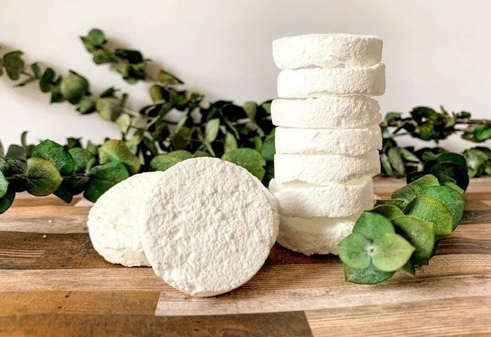 A pile of white cleaning tablets placed next to fresh eucalyptus branches.