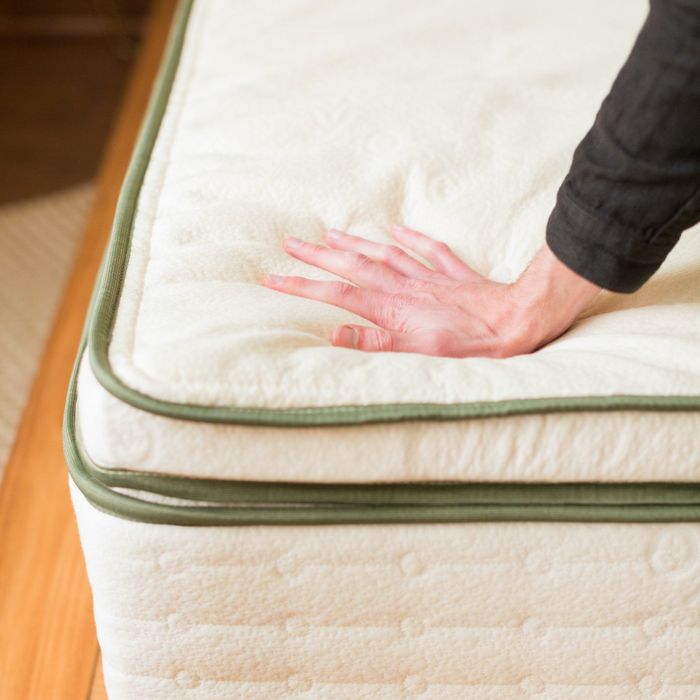 A hand gently presses down on an Avocado green mattress topper.
