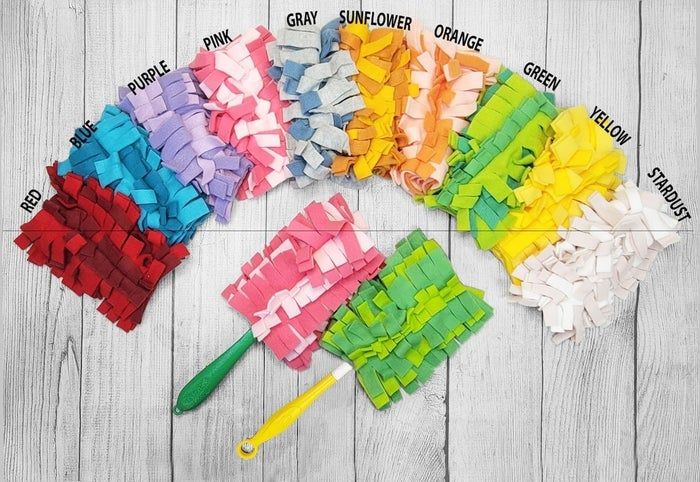 A vibrant collection of yarn samples arranged in a semi-circle, each with a label: red, blue, purple, pink, gray, sunflower, orange, green, yellow, stardust. Two crochet hooks are nearby.