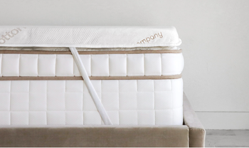 A mattress topper positioned on a mattress, fastened with straps.