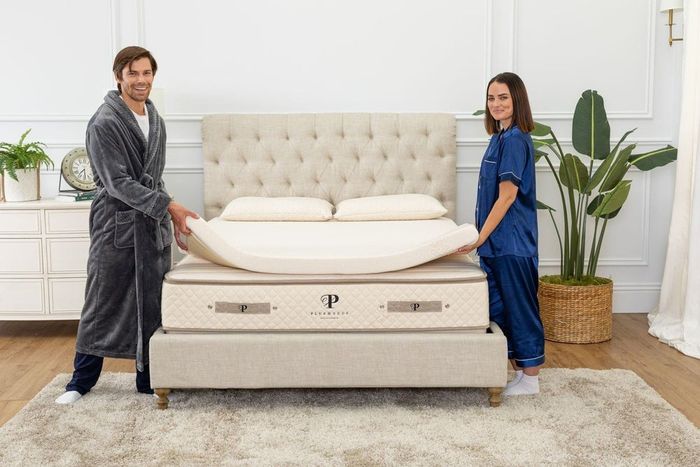 A man and woman placing a mattress topper on top of a mattress.