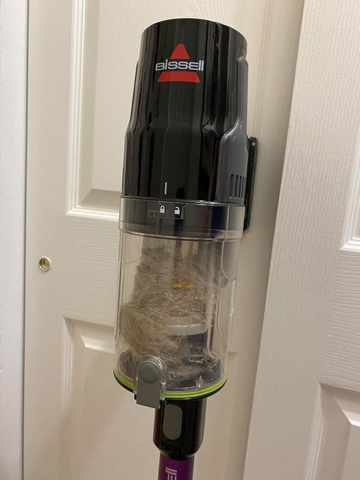 A Bissell vacuum filled with pet hair, hanging neatly on a wall-mounted holder.