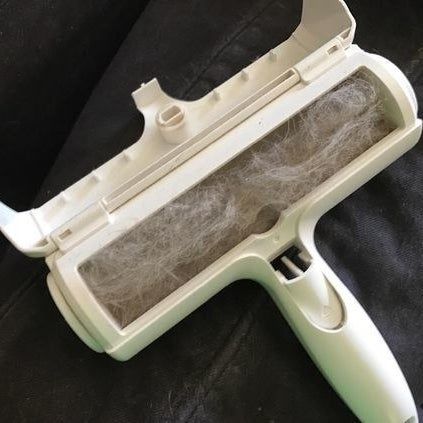 The T-shaped roller with its compartment open, filled with grey pet hair.