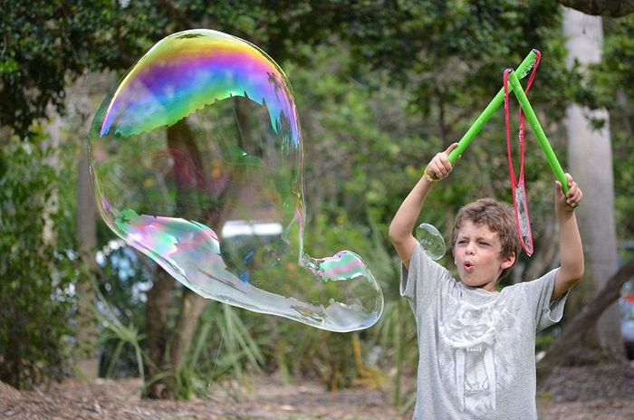 a child holding two bubble wands aloft, creating a giant bubble